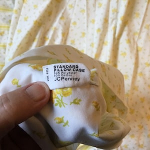 Peut inclure: Une taie d'oreiller standard blanche avec un motif floral jaune. L'&eacute;tiquette en tissu indique : STANDARD PILLOW CASE, 50% Polyester, 50% Cotton, JCPenney, VDR 8312. Le tissu est un m&eacute;lange de polyester et de coton avec un imprim&eacute; de fleurs jaunes.