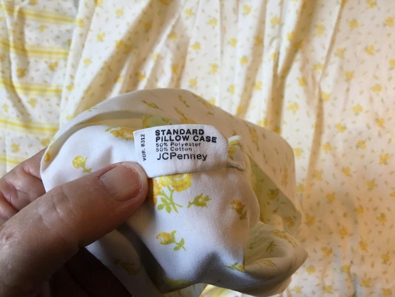 Peut inclure: Une taie d'oreiller standard blanche avec un motif floral jaune. L'&eacute;tiquette en tissu indique : STANDARD PILLOW CASE, 50% Polyester, 50% Cotton, JCPenney, VDR 8312. Le tissu est un m&eacute;lange de polyester et de coton avec un imprim&eacute; de fleurs jaunes.