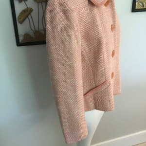 May include: A pink tweed jacket with a collar and button closure. The jacket has a subtle shimmer and a slightly cropped length.