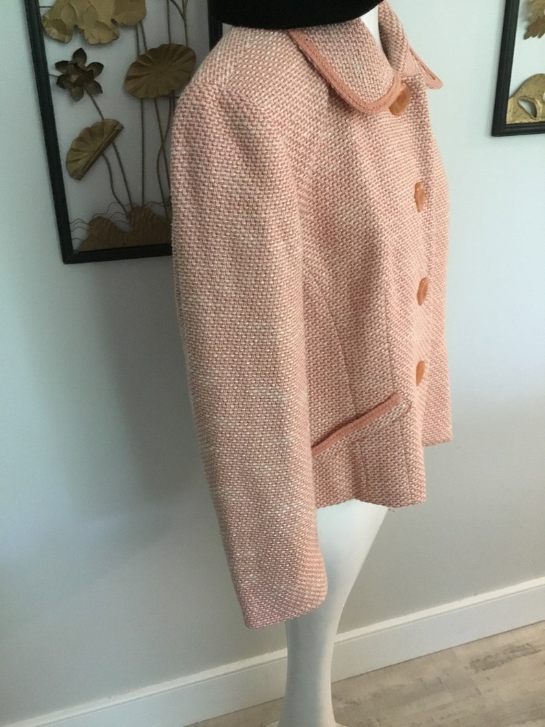 May include: A pink tweed jacket with a collar and button closure. The jacket has a subtle shimmer and a slightly cropped length.