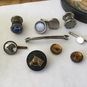 May include: A collection of vintage men's accessories, including cufflinks, tie clips, and buttons. The cufflinks feature blue, white, and iridescent accents. The buttons have a horse head design. The items are silver and gold-toned.