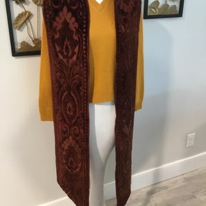 May include: A long brown velvet scarf with an intricate floral pattern. The scarf is displayed on a white mannequin.