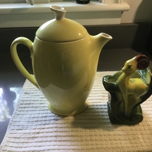 May include: A yellow ceramic teapot with a lid and a matching yellow ceramic planter shaped like a deer with a brown head.
