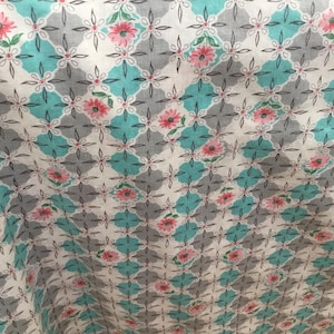 May include: A fabric with a repeating pattern of gray diamonds, turquoise diamonds, and white diamonds. Pink flowers are placed in the center of the turquoise diamonds. The fabric has a floral design.