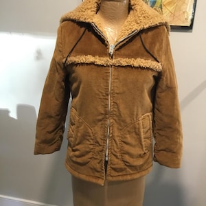 Peut inclure: Une veste en velours côtelé marron avec une capuche doublée de sherpa. La veste a une fermeture éclair et deux poches.