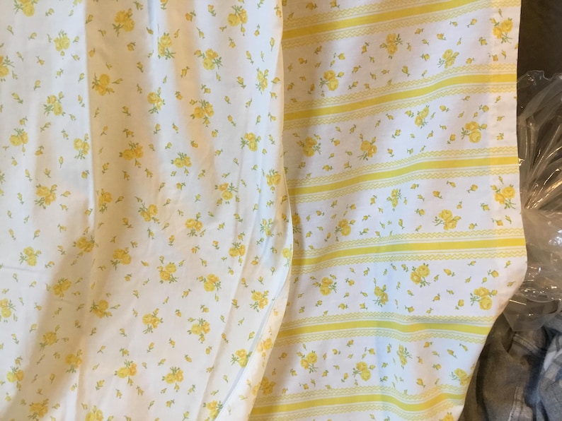 Peut inclure: Un tissu blanc orn&eacute; d'un motif r&eacute;p&eacute;titif de petites fleurs jaunes. Une section pr&eacute;sente un imprim&eacute; floral dense, tandis que la section adjacente comporte des rayures verticales altern&eacute;es de motifs floraux et de fines bandes d&eacute;coratives jaunes.