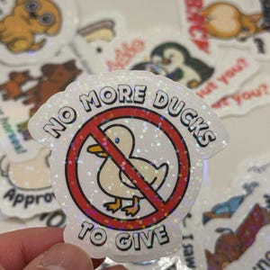 May include: A white sticker with a red circle and a diagonal red line through it. The circle contains a cartoon image of a white duck. The text "NO MORE DUCKS TO GIVE" is printed in black around the circle.