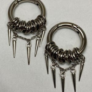May include: Two silver hoop earrings with multiple silver rings and dangling spikes.