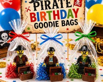 May include: Clear cellophane bags tied with red, blue, and green ribbons, each containing a Lego pirate figure and a treasure chest. A sign reads "Pirate Birthday Goodie Bags" with skull and crossbones balloons in the background.
