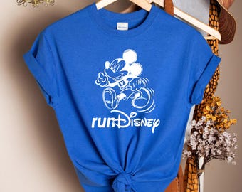 May include: Royal blue t-shirt featuring a white graphic of Mickey Mouse running, with the text "runDisney" below. The shirt is displayed on a wooden hanger.