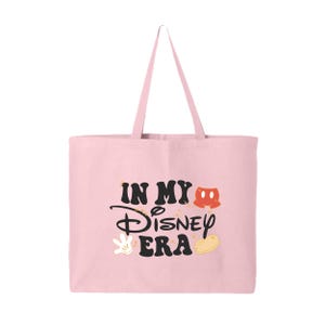 Pu&ograve; includere: Una borsa tote rosa chiaro con manico abbinato. La borsa presenta la scritta "IN MY Disney ERA" in nero, con grafica a tema Mickey Mouse in rosso, bianco e giallo. La borsa &egrave; realizzata in un materiale morbido.