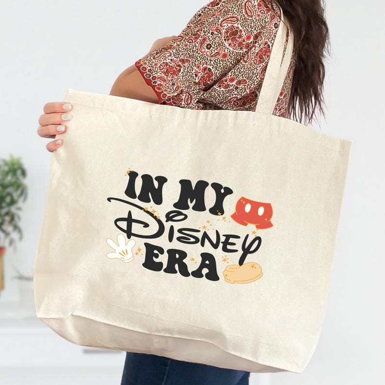 Pu&ograve; includere: Borsa tote color crema con la scritta "IN MY Disney ERA" in nero e oro, insieme a grafiche a tema Mickey Mouse. La borsa ha un design semplice con lunghe cinghie per essere portata a spalla.