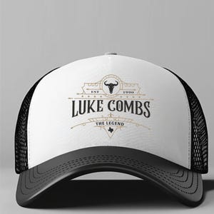 May include: A trucker hat with a white front panel featuring the text "LUKE COMBS" and a bull skull logo. The hat has a black mesh back, a curved black brim, and the text "THE LEGEND" and "EST 1990".