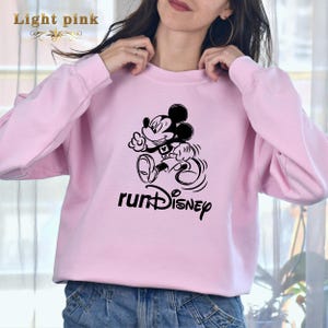 May include: A light pink sweatshirt featuring a black graphic of Mickey Mouse running and the text "runDISNEY".