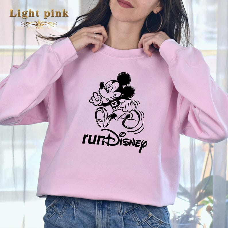 May include: A light pink sweatshirt featuring a black graphic of Mickey Mouse running and the text "runDISNEY".