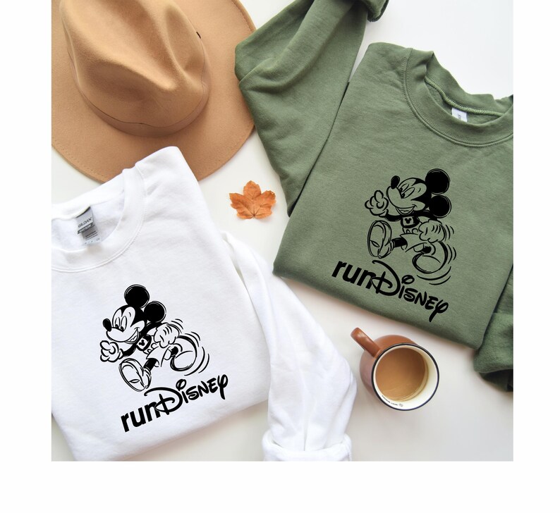 May include: Two white long-sleeved sweatshirts with a black Mickey Mouse graphic and the text "runDisney". One sweatshirt is on a green background and the other is on a brown background.