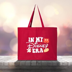 Pu&ograve; includere: Una borsa tote rossa con manici lunghi. La borsa presenta il testo "IN MY Disney ERA" in bianco, insieme a grafiche a tema Mickey Mouse. La borsa &egrave; realizzata in un tessuto robusto ed &egrave; progettata per trasportare oggetti.