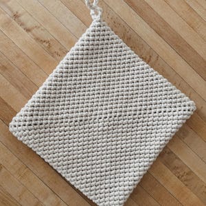 May include: A beige crocheted pot holder with a loop handle. The pot holder is made of a thick, textured yarn and is square in shape.