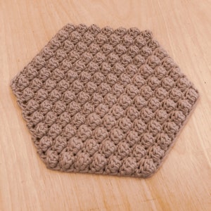 May include: A hexagonal brown crocheted coaster with a textured surface.