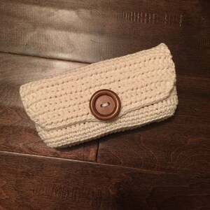 May include: A crocheted clutch purse in a light cream color with a large brown button.