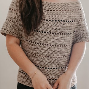 May include: A beige crochet top with a loose, off-the-shoulder fit and short sleeves. The top features a delicate open stitch pattern.