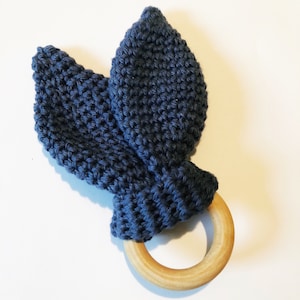 May include: A blue knitted teether with two bunny ears attached to a wooden ring.