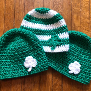 May include: Three crocheted hats in green and white with shamrock designs. The hats are made with a soft, textured yarn.