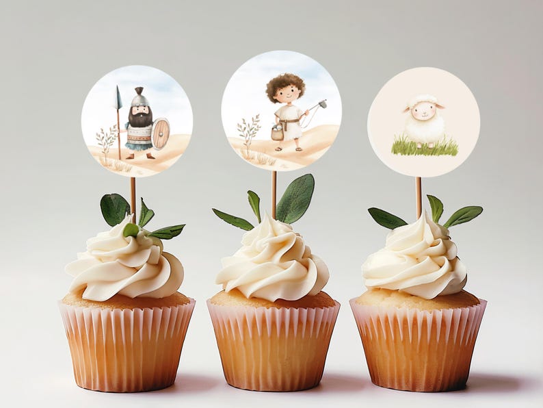 May include: Three cupcakes with white frosting topped with round paper cupcake toppers featuring illustrations of a shepherd, a lamb, and a warrior.