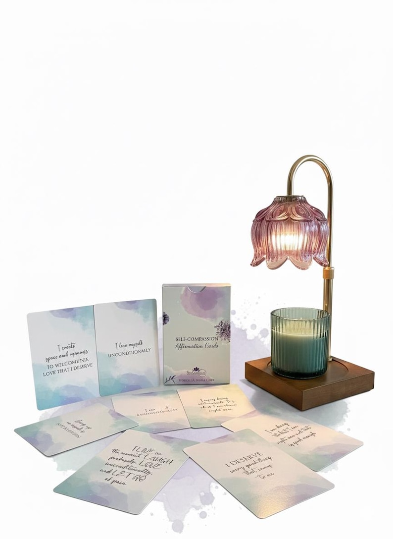 May include: A self-care set featuring affirmation cards, a candle, and a decorative lamp. The cards have inspirational quotes. The lamp has a pink glass shade and a gold-colored metal frame. The candle is in a clear glass holder.