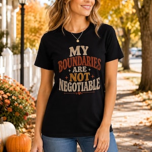 May include: A black short-sleeved t-shirt featuring the text MY BOUNDARIES ARE NOT NEGOTIABLE printed in a distressed font with orange and cream colours, accented by small star symbols and a tiny heart icon centred below the lettering.