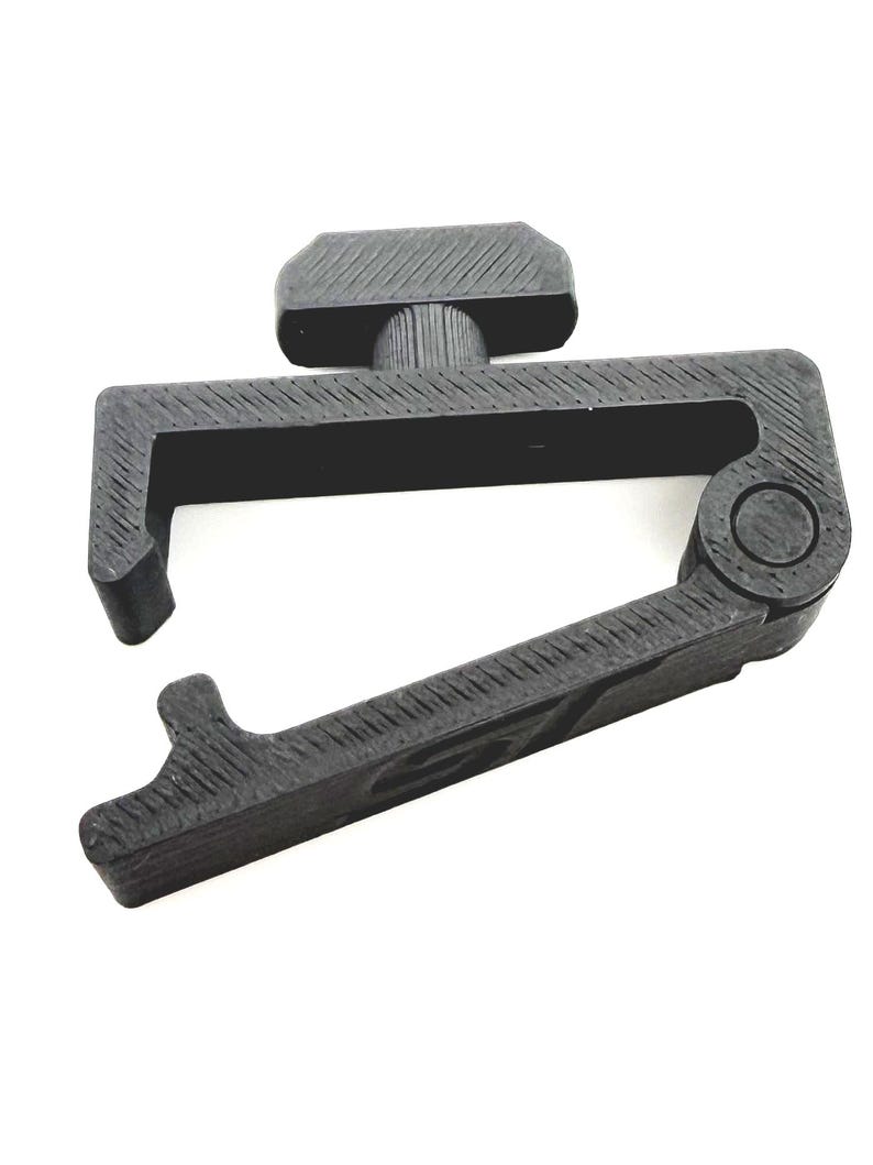 May include: A black capo with a textured surface. The capo has a lever arm and a screw adjustment. The capo is designed to clamp onto the neck of a stringed instrument.