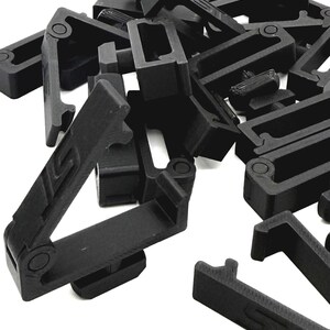 May include: A pile of black plastic clips, each with a rectangular frame and a hinged arm. The clips have a matte finish and are designed to connect or secure items. The image is taken against a white background.