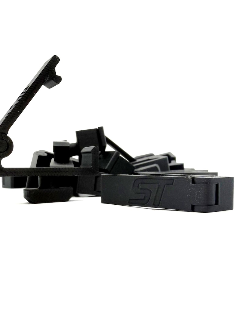 May include: A collection of black plastic clips and fasteners, some with the letters "ST" embossed on them. The objects are scattered against a white background, with a focus on the details of the shapes and textures.