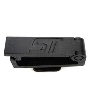 May include: A black, rectangular object with the letters "ST" embossed on the top surface. The object has a hollow interior and a rounded end with a circular detail. The item is made of a matte material.