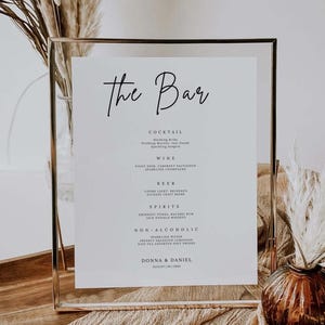 Puede incluir: Un menú de bar enmarcado con la frase "The Bar" en escritura elegante. El menú enumera cócteles, vinos, cervezas, licores y bebidas sin alcohol. La parte inferior del menú incluye los nombres Donna & Daniel y la fecha 20 de agosto de 2025.