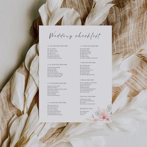 Puede incluir: Una lista de verificación de boda en papel blanco con un diseño floral. El texto "Wedding checklist" está en la parte superior. La lista incluye tareas para 18, 12, 9, 6, 3 y 1 mes antes de la boda, más 1 semana y el día de la boda.