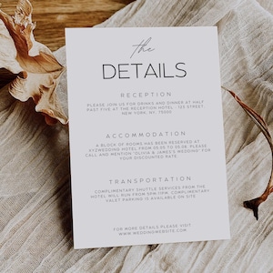 May include: A white invitation card with the text "the DETAILS" in a minimalist font. The card includes details about a reception, accommodation, and transportation. The card is on a beige fabric surface.