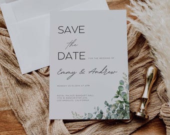Può includere: Un invito di nozze con il testo "Save the Date" e i nomi "Emmy & Andrew". L'invito è bianco con accenti floreali verdi e un sigillo di cera dorata. Una busta è visibile sullo sfondo.