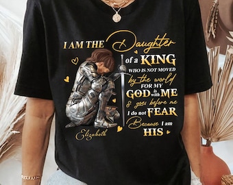 May include: A black short-sleeve t-shirt featuring a graphic of a knight in silver armor kneeling with a sword. The text reads: I AM THE Daughter of a KING WHO IS NOT MOVED by the world FOR MY GOD is with ME & goes before me I do not FEAR Because I am HIS Elizabeth.