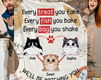 Könnte beinhalten: Eine cremefarbene Decke mit drei Cartoon-Katzen und dem Text "Every treat you fake, Every fish you bake, Every bag you shake, We'll be watching you." Die Katzen heißen Sam, Janet und Sophia. Die Decke hat ein Herz- und Pfotenabdruck-Design.