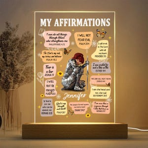 May include: An illuminated acrylic sign with the words "MY AFFIRMATIONS" at the top. The sign features a kneeling figure in armor, surrounded by inspirational quotes and floral accents. The base is made of wood.