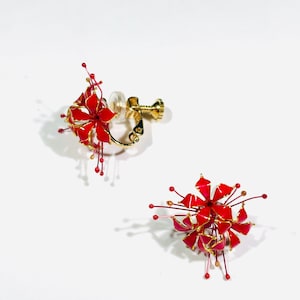 K&ouml;nnte beinhalten: Ein Paar Clip-Ohrringe mit floralem Design. Die Ohrringe sind &uuml;berwiegend rot mit goldenen Akzenten und feinen Drahtdetails. Der Clip-Mechanismus ist goldfarben.