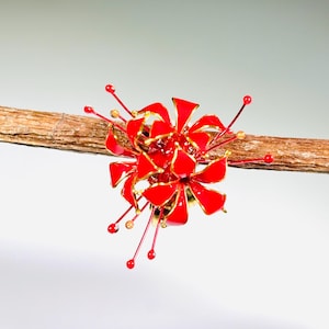 K&ouml;nnte beinhalten: Ein rotes und goldenes Blumenornament mit detailliertem Design. Das Ornament ist an einem braunen Zweig befestigt, mit roten und goldenen Akzenten. Die Blume hat ein detailliertes, geschichtetes Design.