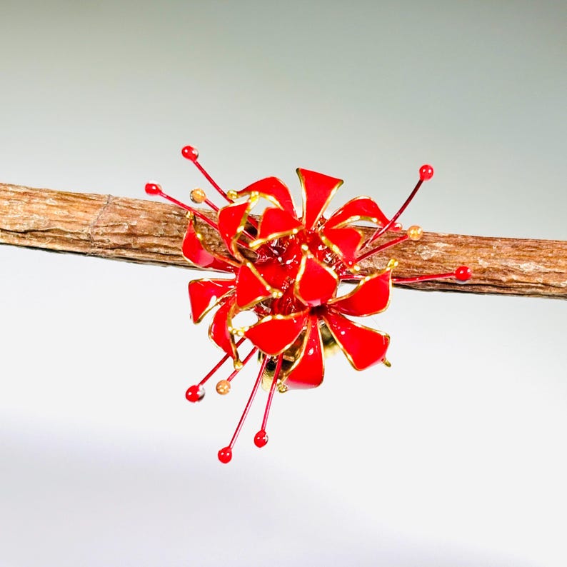 K&ouml;nnte beinhalten: Ein rotes und goldenes Blumenornament mit detailliertem Design. Das Ornament ist an einem braunen Zweig befestigt, mit roten und goldenen Akzenten. Die Blume hat ein detailliertes, geschichtetes Design.
