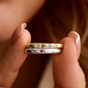 Könnte beinhalten: Zwei filigrane Ringe werden gezeigt. Der obere Ring ist goldfarben mit kleinen, farbigen Edelsteinen. Der untere Ring ist silberfarben mit einem einzelnen roten Edelstein. Die Ringe gehören wahrscheinlich zur Kategorie Schmuck.