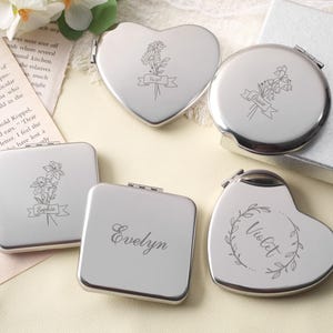 May include: A collection of five silver-toned metal compact mirrors in heart, round, and square shapes. Each mirror features a unique laser-engraved design, including floral illustrations and the names Hazel, Grace, Sophia, Evelyn, and Violet.