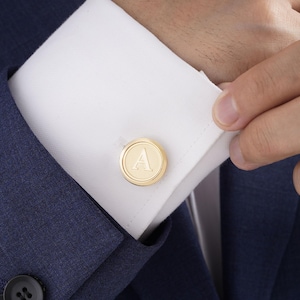May include: Gold cufflinks with a raised letter 'A' in the center.