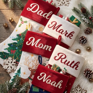 Puede incluir: Cinco calcetines de Navidad con los nombres bordados Dad, Mark, Mom, Ruth y Noah. Los calcetines están hechos de tela roja y blanca con diseños festivos que incluyen un árbol de Navidad, un reno y Santa Claus, cada uno con un lazo para colgar.