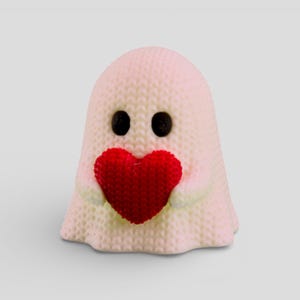 A small, white ghost figurine holding a red heart-shaped object in its hands.