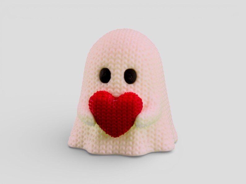 A small, white ghost figurine holding a red heart-shaped object in its hands.